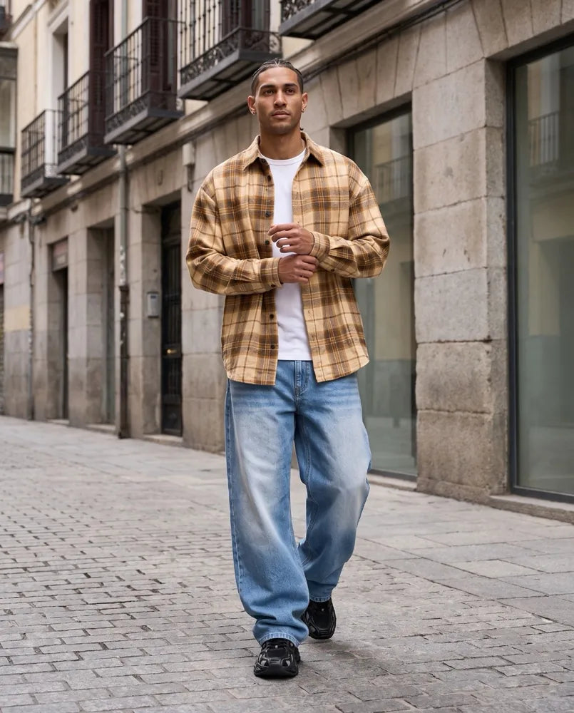 Hombre con sobrecamisa de cuadros, camiseta blanca y vaqueros anchos caminando por una calle europea